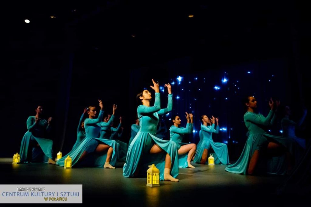 Na scenie w niebieskich sukienkach tancerki klęczące obok lapiony.