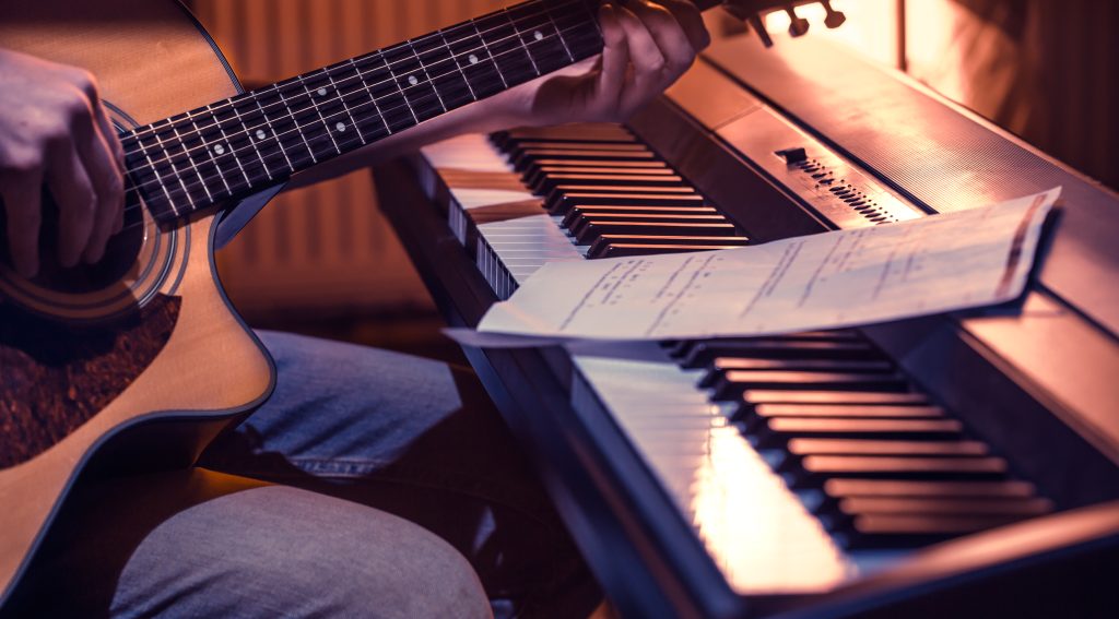 Na zdjęciu mężczyzna grająca na gitarze akustycznej, siedzący przy pianinie