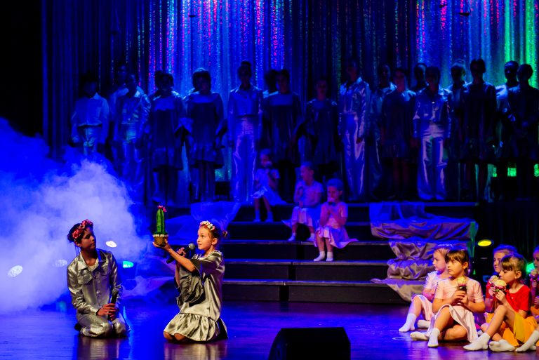Widowisko taneczno-muzyczne "Mam tę moc" -dwie dziewczynki w srebrnych strojach śpiewają piosenkę, jedna z nich trzyma kaktusa.