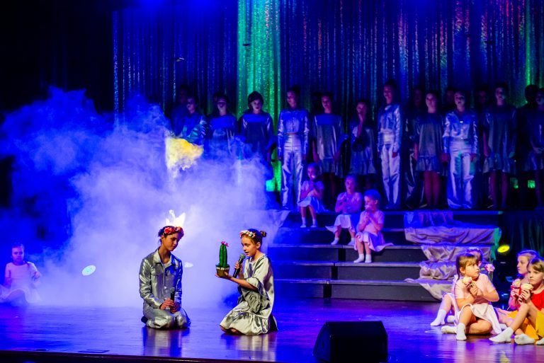 Widowisko taneczno-muzyczne "Mam tę moc" -dwie dziewczynki w srebrnych strojach śpiewają piosenkę, jedna z nich trzyma kaktusa.