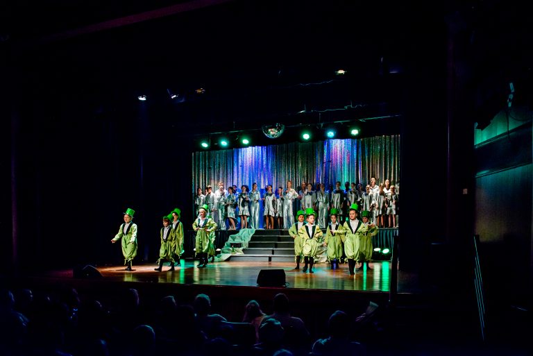 Widowisko taneczno-muzyczne "Mam tę moc" - grupa chórzystów stojąca z tyłu i grupa dziewczynek w zielonych garniturkach śpiewają piosenkę