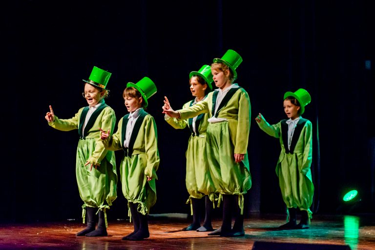Widowisko taneczno-muzyczne "Mam tę moc" - grupa chórzystów stojąca z tyłu i grupa dziewczynek w zielonych garniturkach śpiewają piosenkę