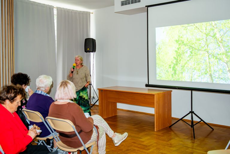 Na zdjęciu kobieta omawiająca prezentację oraz cztery siedzące na krzesłach osoby