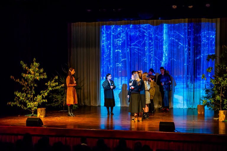 Na zdjęciu grupa młodych ludzi znajdująca się na scenie, odgrywająca scenę ze spektaklu