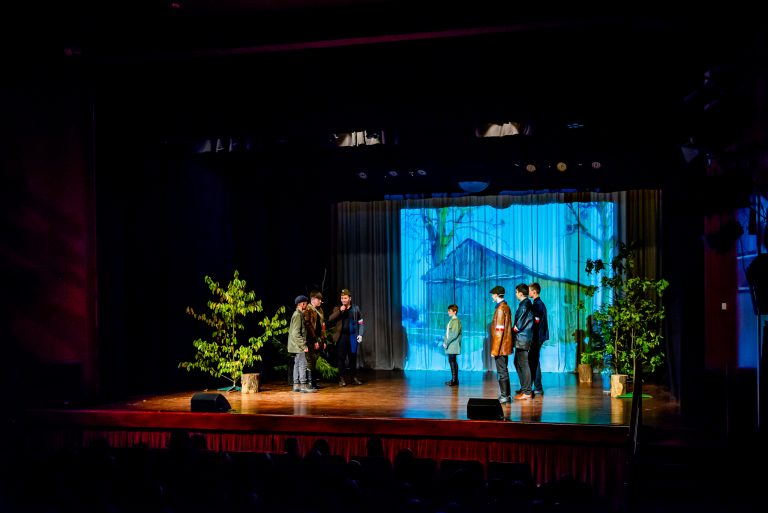 Na zdjęciu grupa młodych ludzi znajdująca się na scenie , odgrywająca scenę ze spektaklu