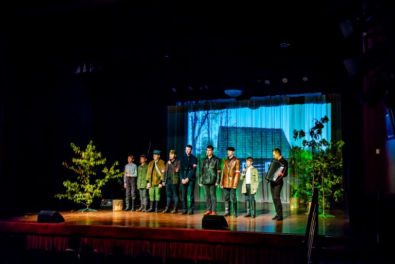 Na zdjęciu grupa młodych ludzi znajdująca się na scenie , odgrywająca scenę ze spektaklu