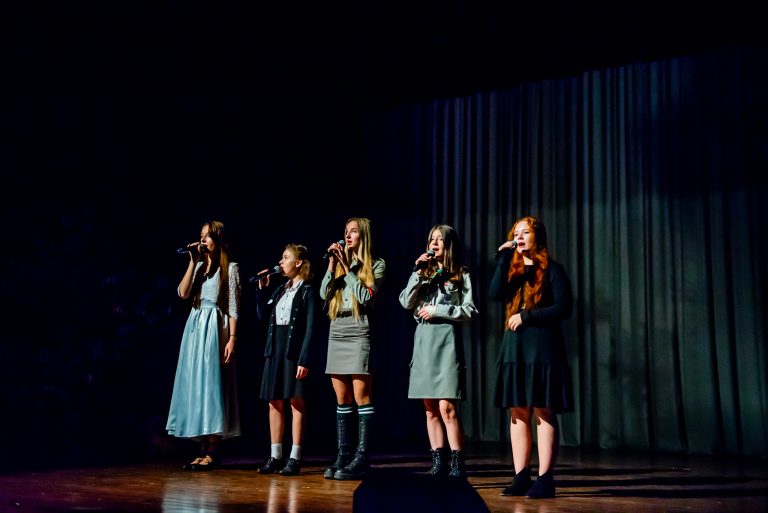 Na zdjęciu grupa dziewcząt śpiewająca piosenkę do mikrofonów