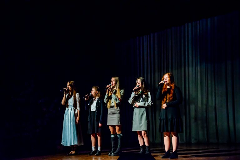 Na zdjęciu grupa dziewcząt śpiewająca piosenkę do mikrofonów