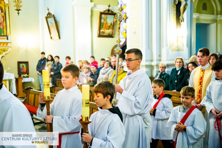 Zdjęcie przedstawia ministrantów trzymających świece i krzyż