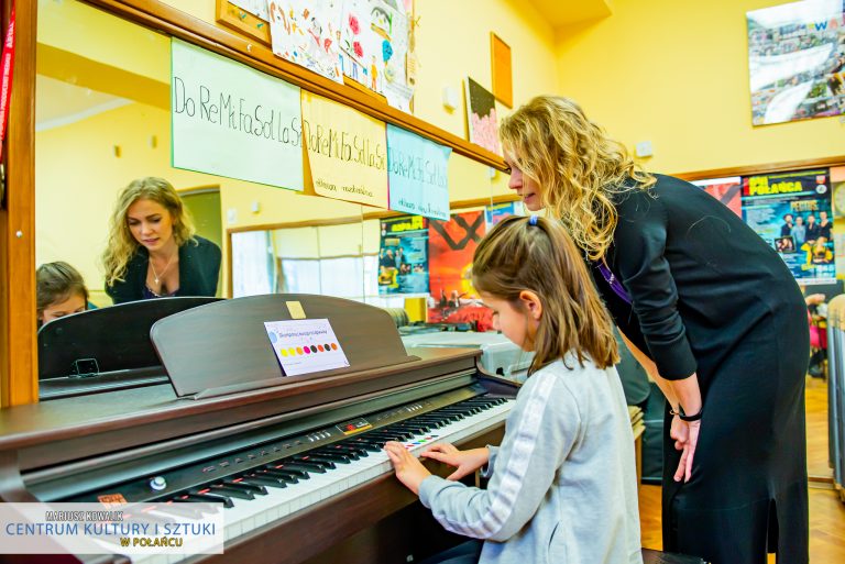 Dziewczynka gra na pianinie skomponowaną przez siebie melodię, kobieta nachyla się nad nią i jej pomaga