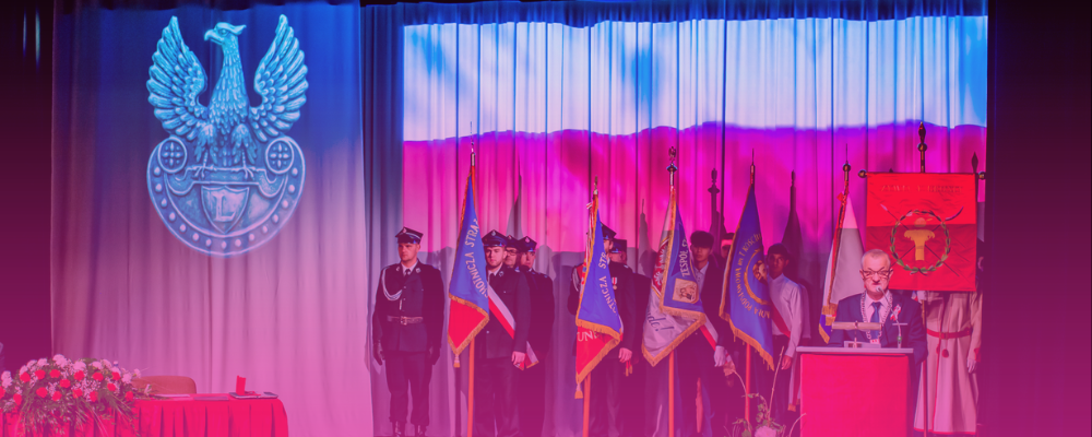 Na zdjęciu grupa ubranych w mundur i stojących na baczność mężczyzn oraz stojący przy mównicy mężczyzna. W tle flaga i godło Polski