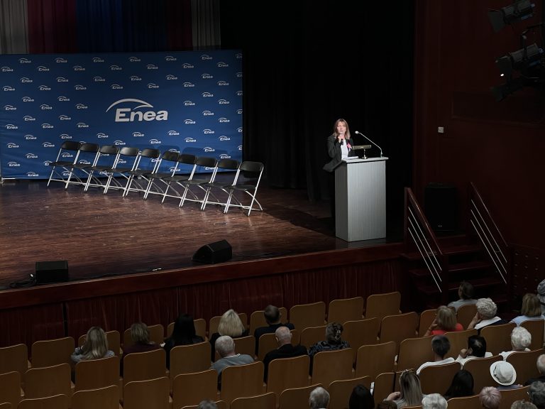 Na zdjęciu kobieta stojąca na scenie przy mównicy - w tle baner Enea