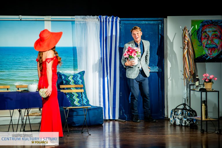 Aktorzy spektaklu komediowego "Miłosna Pułapka" odgrywają scenę - mężczyzna wchodzi do pokoju kobiety z kwiatami
