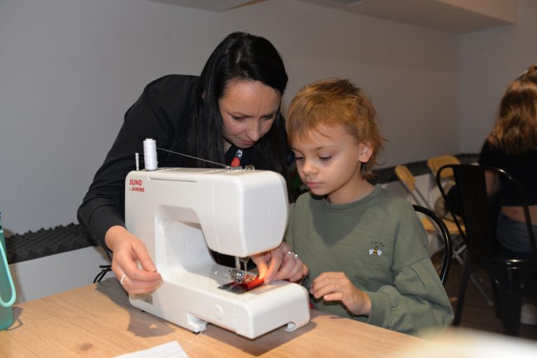 Warsztaty krawieckie - instruktor pomaga dziewczynce przy maszynie do szycia