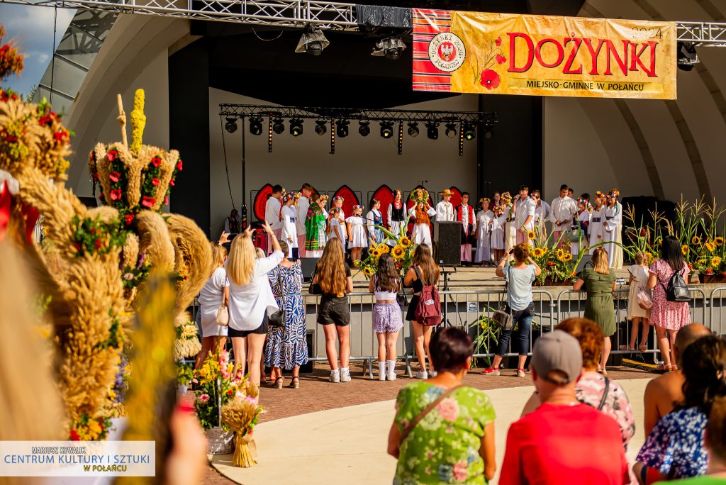 Scena z "Misterium Żniwnego", zdjęcie z oddalenia. Nad sceną baner "dożynki 2024", a po lewej stronie fragment wieńców dożynkowych 