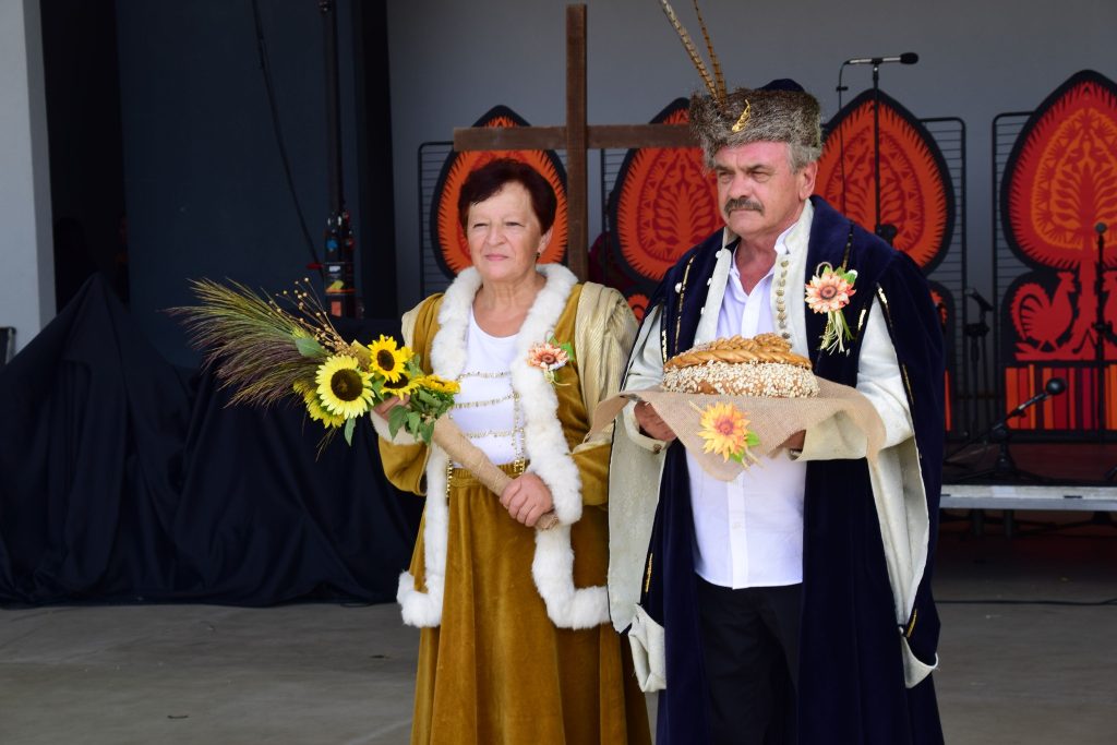 Starosta i Starościna dożynek, trzymający dary natury - bukiet ze zbóż i słoneczników oraz chleb 