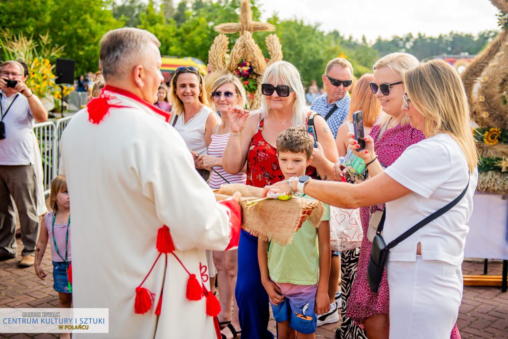 Burmistrz Miasta i Gminy Połaniec rozdający mieszkańców obecnym na wydarzeniu chleb. Po chleb sięgają uśmiechnięte kobiety oraz mały chłopiec